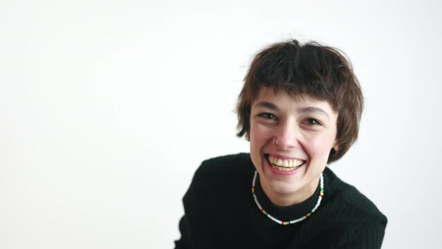 Short-haired tomboy girl voguing at camera with two hands and bursting in laughter. Isolated studio shot over white background. Copy space. High quality 4k footage