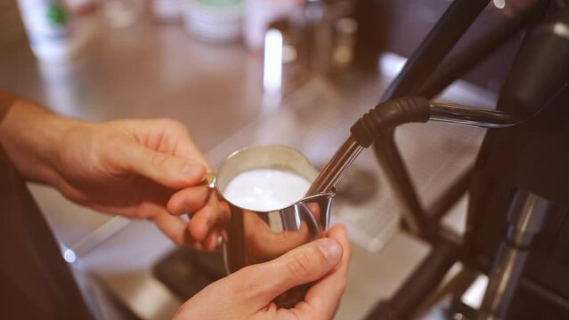 barista heating fresh milk for making cappuccino or latte coffee hot drink