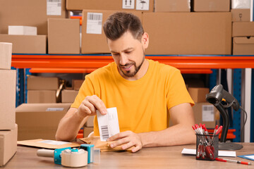 Post office worker sticking barcode on parcel at counter indoors