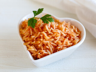 Tomato onion rice, Tamatar Biryani, jollof in white heart shape bowl on a white wooden table, horizontal. Love valentine day dinner concept