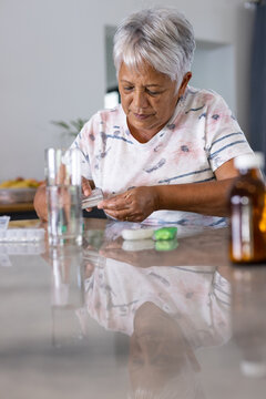 Biracial senior woman with gray short hair taking prescribed medicines on table at home, copy space