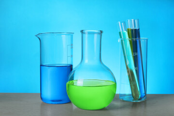 Different laboratory glassware with colorful liquids on wooden table against light blue background