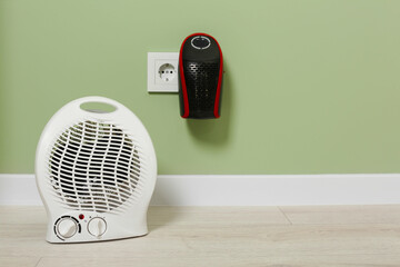 Different electric heaters near pale green wall indoors. Space for text
