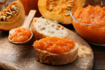 Slices of bread with delicious pumpkin jam and fresh pumpkin on wooden table, closeup