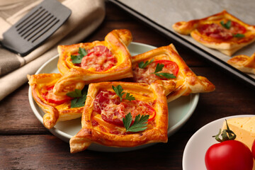 Fresh delicious puff pastry with cheese, tomatoes and parsley on wooden table, closeup
