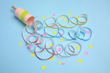 Beautiful serpentine and confetti bursting out of party popper on light blue background