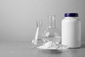 Plate with calcium carbonate powder, jar and laboratory glassware on grey table. Space for text