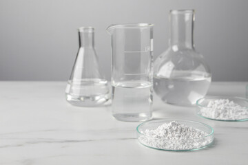 Petri dishes with calcium carbonate powder and laboratory glassware on white marble table. Space...