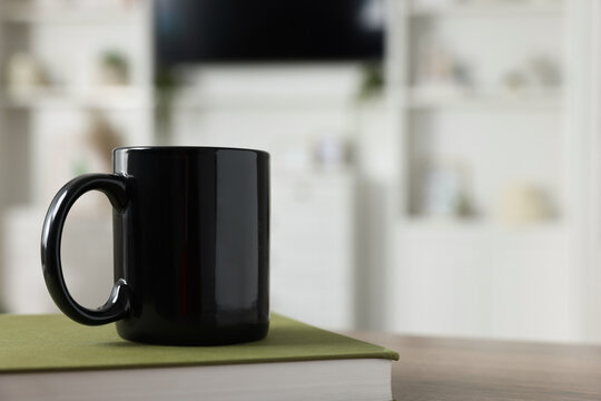 Blank ceramic mug and book on wooden table. Mockup for design