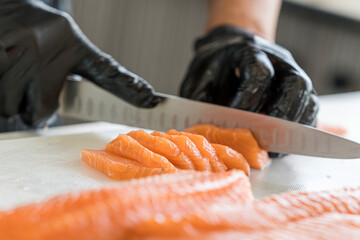 Japanese Chef preparing a fresh salmon fillet in kitchen. Close up hand of chef with salmon sashimi. - obrazy, fototapety, plakaty