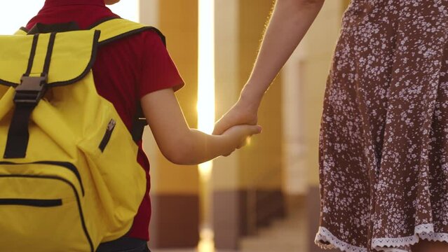 mother leads hand child kid with school backpack sunset. happy family. education concept. view from back. hands sunshine. little boy child goes with his mother school building with school bag back