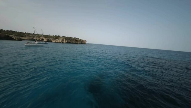 FPV drone shot of steep cliffs and natural stone bridge along the seaside in Cala Varques, Mallorca, Spain during evening time.