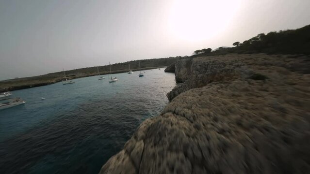 FPV drone shot along seaside with steep rocky cliffs in Cala Varques, Mallorca Island, Balearic islands, Spain on a bright sunny day.