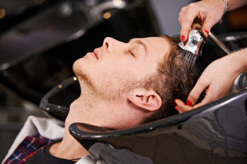 Its always a very relaxing experience. a young man having his hair washed at a hair salon.