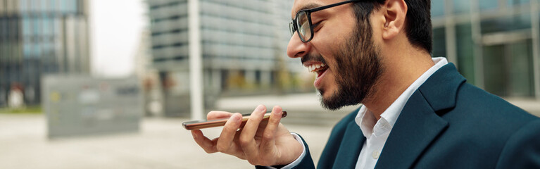 Fototapeta premium Indian Businessman is recording audio message to client standing near office during break