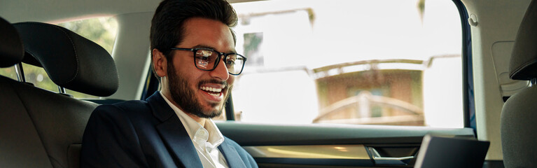 Attractive businessman in suit working laptop while riding in car to office