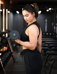 Fit and Young Indian Girl Lifting Dumbell doing Bicep Curls for strong arms and flexing at the Gym.