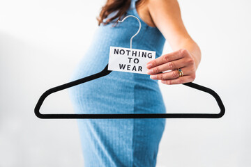 maternity wear and inclusive fashion, Nothing to Wear sign held by pregnant woman in the last month of pregnancy wearing stretchy blue dress showing her bump