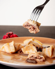 raviol pasta rellena relleno de carne pinchado con tenedor sobre mantel negro y fondo blanco