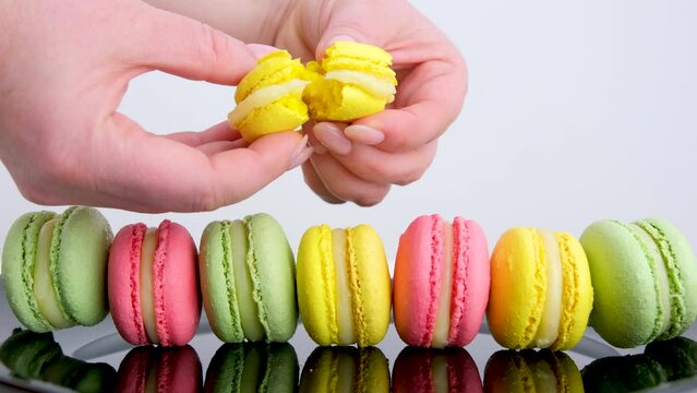 female hands breaking yellow lemon macarons Line of yellow pink and green macaroons colourful pastel macarons isolated on white background Macaron colorful on table 