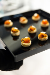 The waiter holds a Set of festive appetizer canapes on bread on a black tray as an event dish. Buffet table. Catering. Delicacy. Haute cuisine. 