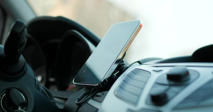 Close Up Shot Of Mounting Smartphone On Magnetic Dashboard Holder Beside Steering Wheel Inside Car. Locked Off