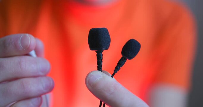 Person showing the camera 3 types of tie microphones. Blurred background.