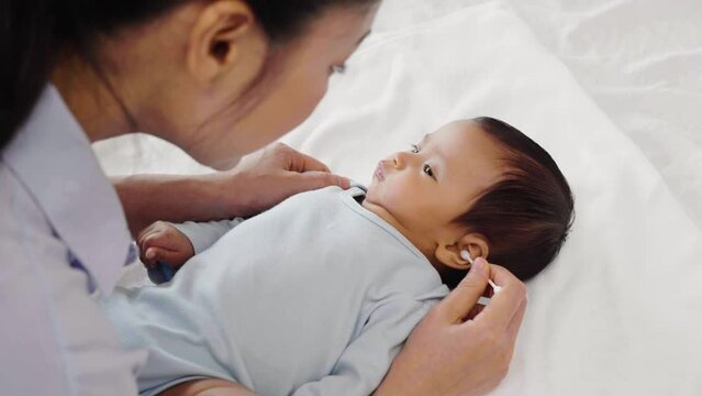 mother using cotton bud to cleaning ear of newborn baby on a bed