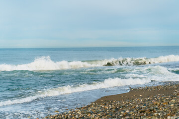small waves on the shore of a pebble beach. The sea coast in cloudy weather.