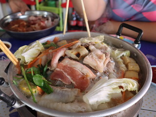 close up image hand-hold chopsticks whit Korean bbq Thai-style hot pot,  Moo Kra Ta (Thai word)