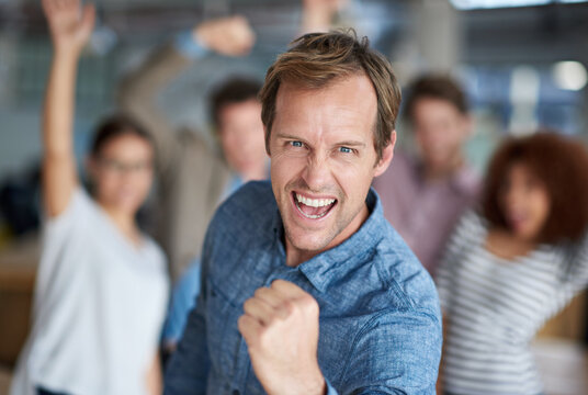 Hell yeah We did it. Mature man shouting triumphantly and making a fist with celebrating staff in the background.