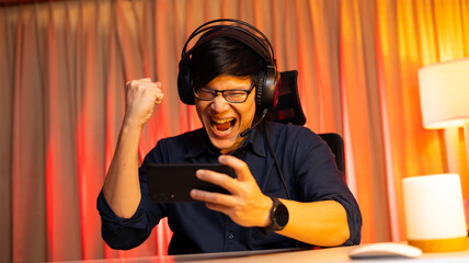 Esport online games. Happy and excited asian man gamer playing online game on smartphone. Colorful neon light room. Esport online game. © NVB Stocker