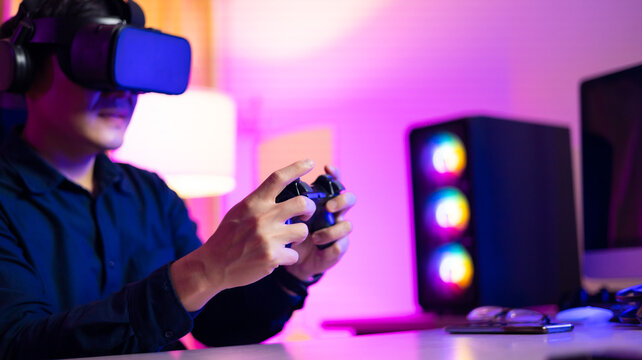 VR Headset. Asian man playing game on mobile phone with 3D simulation VR headset. Colorful neon light room. Esport online game.