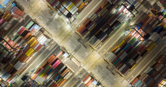 Aerial drone time-lapse top view over container terminal port loading and unloading to ship at night. Industrial shipyard being loaded containers onto a freight. import export global supply chain.