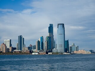 Fototapeta premium Looking back on Manhattan from the Hudson River and Liberty Island, as the towering high rises of Lower Manhattan loom above the river