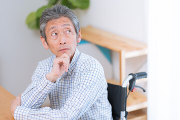 車椅子に乗った考えるシニア男性（介護・福祉）