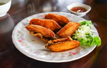 The close up picture of batter fried chicken wings in Thai style with salad served on a white dish and Thai sweet chili dipping chicken sauce in a restaurant.