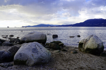 Fototapeta na wymiar View of ships moored in English Bay from Kitsilano Beach with boulders in the foreground in the late afternoon