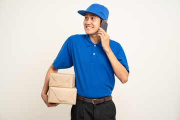 Asian man in blue uniform standing holding box parcel cardboard and smartphone on isolated white background. Male service worker with cell phone. Delivery courier shipping service
