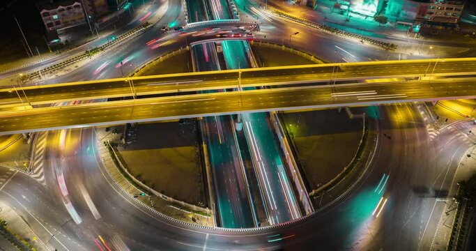 Aerial drone time-lapse of urban traffic on street intersection freeway road in capital city. Circle roundabout transportation cityscape with streaking light trail at night. High angle view timelapse.