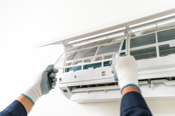 Air conditioner service indoors. Air conditioner cleaning technician He opened the front cover and took out the filters and washed it. He in uniform wearing rubber