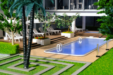 Close up view of modern contemporary miniature model of luxury housing with swimming pool. Focus on the pool deck chairs. Construction, home architecture, property and real estate concept
