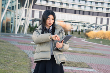 Business time management.Portrait of a young woman who watches the time on her wristwatch and holds a laptop