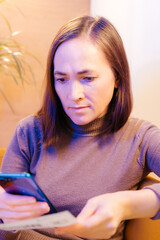 A woman is resting in a cozy soft chair with a smartphone. Pretty smiling woman is looking at the screen of the device, and is typing. Social media fun