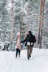 Fototapeta na wymiar A man and a woman run through the winter forest. Happy family run hand in hand through the snowy park.