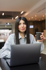 A young freelance woman drinks coffee while working at a laptop in a cafe