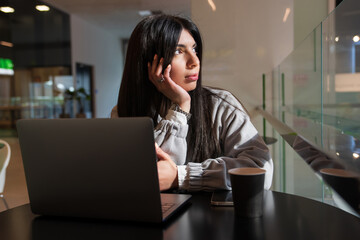 A dreaming woman is sitting in a cafe with a laptop. Rest from work. Time for reflection