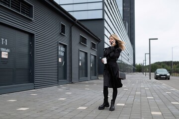 young woman speaks on the phone against the backdrop of a strong office building