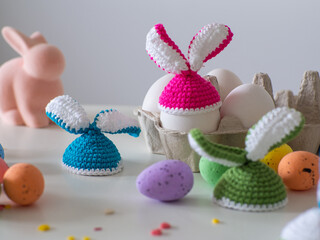 Colotful crochet hats with ears for Easter eggs. Crocheted hat with bunny ears. Easter Greeting card. Happy Easter holiday concept with cute handmade eggs with knitted bunny hats with copy space.