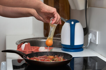 Cooking scrambled eggs with ham. Breaking an egg